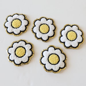May include: Five white felt daisy flower patches with yellow centers and gold glitter around the edges.