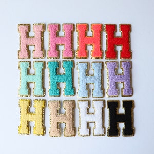 May include: Nine felt letter patches in various colors, each with a gold outline, spelling out the letter "H". The colors include pink, coral, light blue, turquoise, lavender, yellow, beige, white, and black.