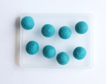 May include: Eight teal blue felt balls arranged in a clear plastic tray.