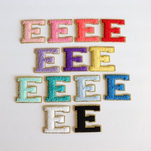 May include: A set of ten felt letter patches in various colors, including pink, red, purple, yellow, light blue, teal, blue, white, and black. Each patch features the letter "E" in a gold outline.
