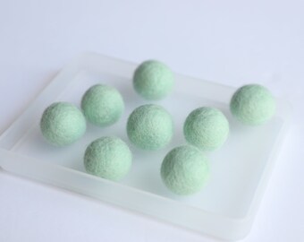May include: Eight light green felt balls arranged in a clear plastic tray. The balls are soft and round.