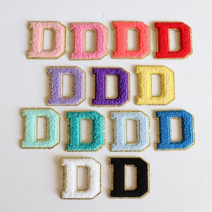 May include: A set of 12 felt letter patches in various colors, each featuring the letter "D" in a gold outline. The colors include pink, red, lavender, purple, yellow, light blue, teal, blue, white, and black.