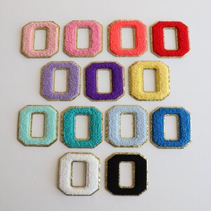 May include: Ten felt patches in various colors, each shaped like a letter O with a gold outline. The patches are arranged in three rows.