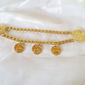 May include: A gold chain belt with three round, decorative charms. The chain is linked together with a thick, gold chain.