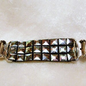 May include: A silver metal garment clip with a row of silver pyramid-shaped studs. The clip is designed to hold fabric together.