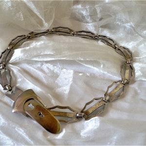 May include: A silver metal belt with a unique geometric design and a large, ornate buckle.