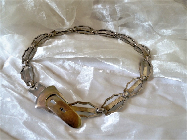 May include: A silver metal belt with a unique geometric design and a large, ornate buckle.