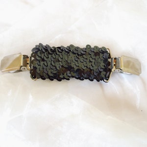 May include: A black sequined fabric strip with silver metal clips on each end. The strip is about 5 cm wide and 12.5 cm long.