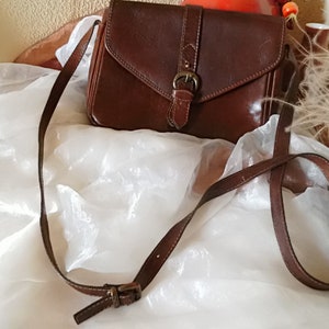 May include: A brown leather crossbody bag with a flap closure and a metal buckle. The bag has a long adjustable strap.