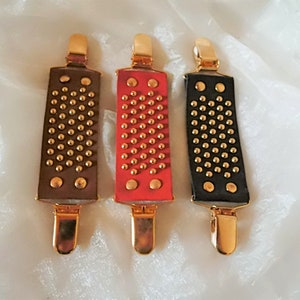 May include: Three leather belt clips with gold metal clasps and gold studs. The clips are brown, red, and black.