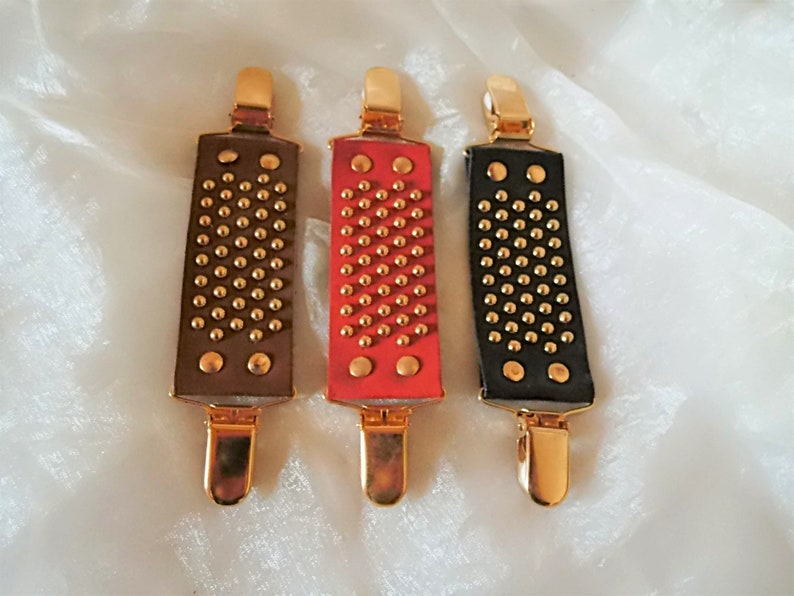 May include: Three leather belt clips with gold metal clasps and gold studs. The clips are brown, red, and black.