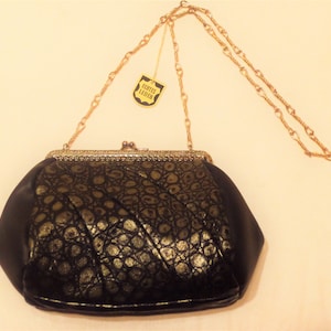 Pode incluir: Uma carteira de mão preta e dourada com uma alça de corrente dourada. A carteira tem um design texturizado, com relevo de crocodilo e uma etiqueta que diz "Echtes Leder".