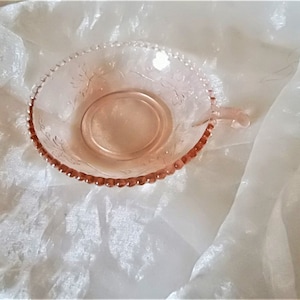 Könnte beinhalten: Eine rosa Glasschüssel mit einem gewellten Rand und einem einzelnen Griff. Die Schüssel hat ein Blumenmuster und ist perfekt zum Servieren von Snacks oder Desserts.