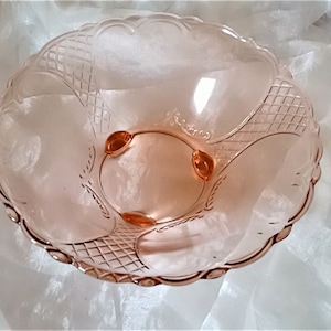 Könnte beinhalten: Eine rosa Glasschüssel mit einem gewellten Rand und einem Rautenmuster. Die Schüssel hat drei Füße und ist aus klarem Glas.