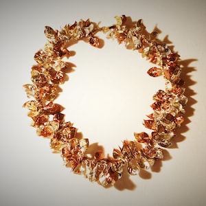 May include: A gold and copper coloured garland made of metal leaves. The garland is in the shape of a circle.
