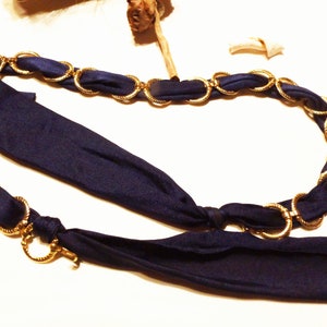 May include: A gold chain necklace with a navy blue fabric ribbon tied in a knot. The chain is made of linked oval rings.