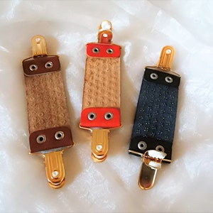 May include: Three leather razor strop holders with gold metal clips. The strops are brown, red, and black.