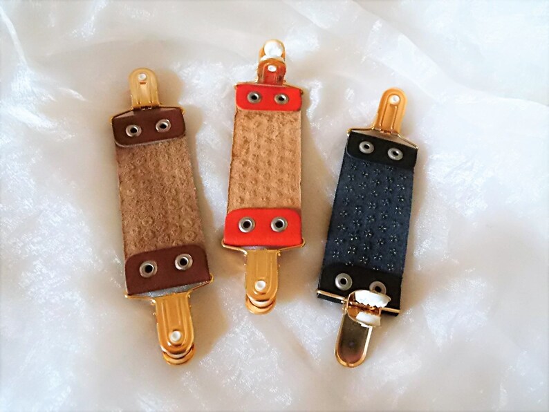 May include: Three leather razor strop holders with gold metal clips. The strops are brown, red, and black.