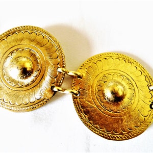 Puede incluir: Un cintur&oacute;n dorado con medallones redondos, ornamentados y decorativos. Cada medall&oacute;n tiene un centro elevado y un dise&ntilde;o de c&iacute;rculo conc&eacute;ntrico.