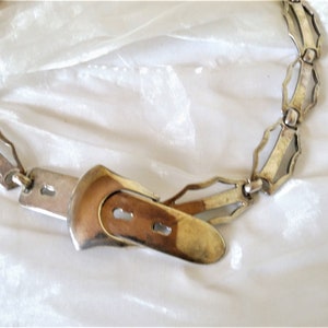 May include: A silver chain belt with a decorative buckle. The chain is made of interlocking links with a geometric design. The buckle is a simple, rectangular shape.