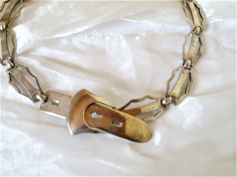 May include: A silver chain belt with a decorative buckle. The chain is made of interlocking links with a geometric design. The buckle is a simple, rectangular shape.
