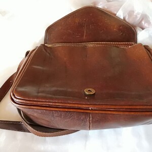 May include: A brown leather shoulder bag with a flap closure and a single strap. The bag has a metal button closure and a smooth leather finish.