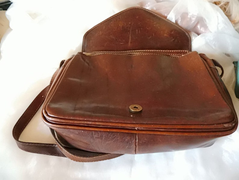 May include: A brown leather shoulder bag with a flap closure and a single strap. The bag has a metal button closure and a smooth leather finish.