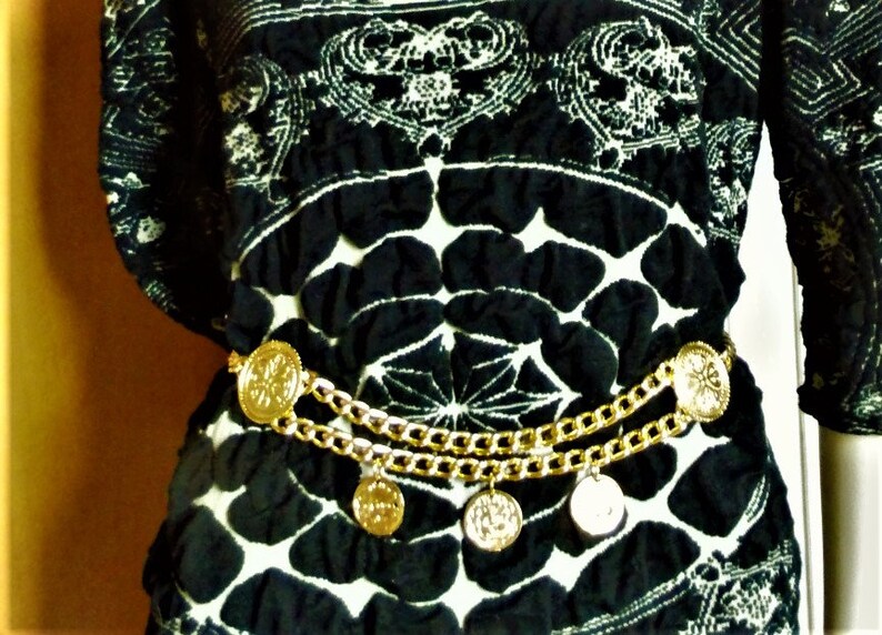 May include: A black and white patterned blouse with a gold chain belt featuring round medallions.