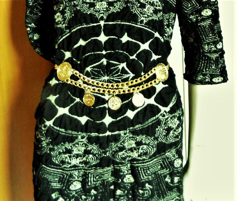May include: A black and white patterned dress with a gold chain belt featuring decorative coin-like charms.