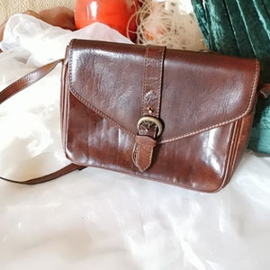 May include: A brown leather crossbody bag with a flap closure and a silver buckle. The bag has a long adjustable strap.