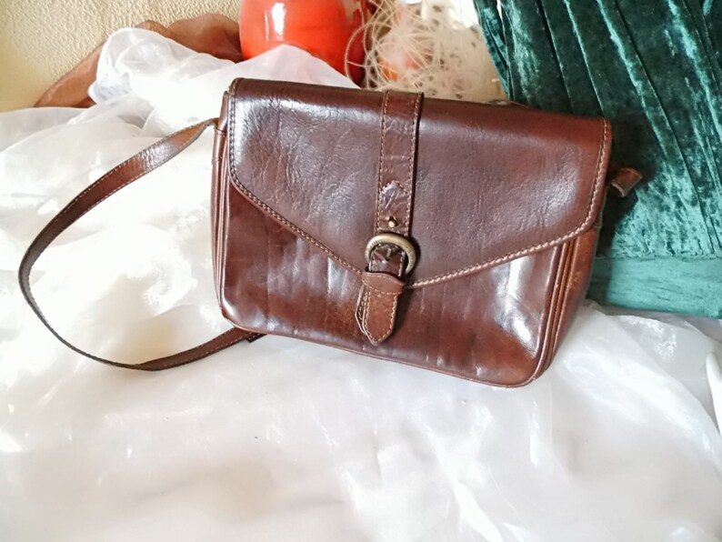 May include: A brown leather crossbody bag with a flap closure and a silver buckle. The bag has a long adjustable strap.
