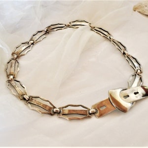 May include: A silver chain belt with a decorative buckle. The chain is made of interlocking links with a geometric design.