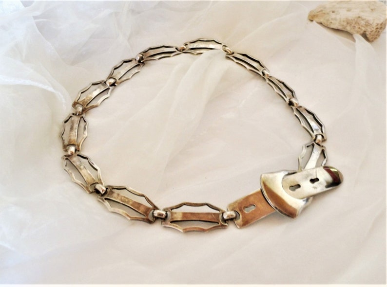 May include: A silver chain belt with a decorative buckle. The chain is made of interlocking links with a geometric design.