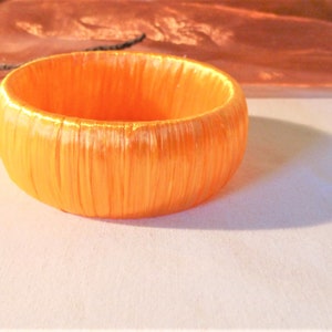 Könnte beinhalten: Ein leuchtend orangefarbenes Armband aus gewebtem Stoff.