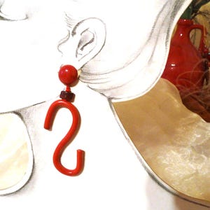May include: Red and brown statement earrings with a large, curved, red hook shape.