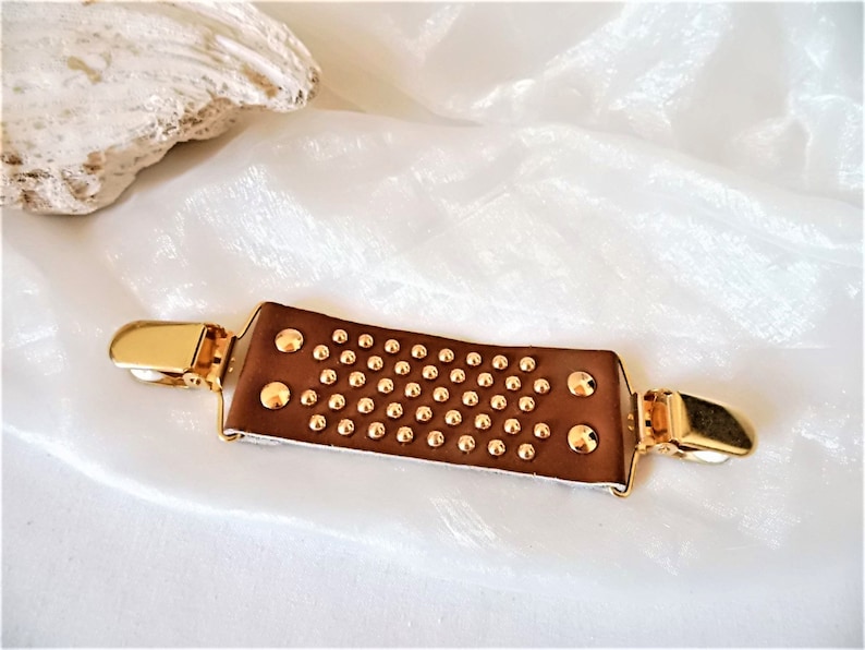 May include: A brown leather garment clip with gold metal accents and a studded design.