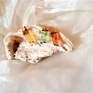 K&ouml;nnte beinhalten: Vier Paar H&auml;ngeohrringe mit goldenen Haken und langen, rechteckigen, durchsichtigen Steinen. Die Steine sind in den Farben Bernstein, Gr&uuml;n und Orange.