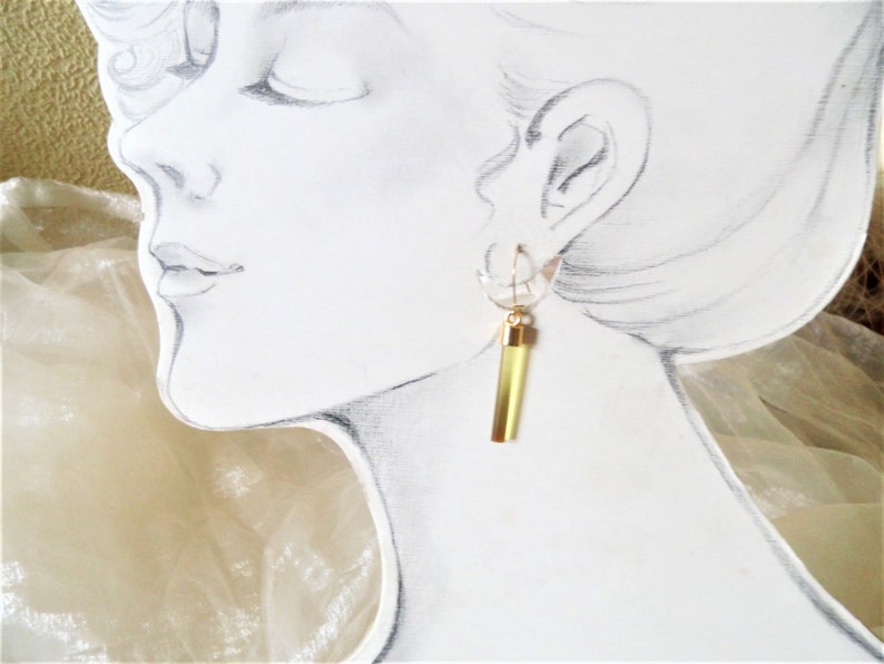 K&ouml;nnte beinhalten: Ein Paar goldene Ohrringe mit einem durchsichtigen Glasr&ouml;hrchen, das mit einer gelben Fl&uuml;ssigkeit gef&uuml;llt ist.