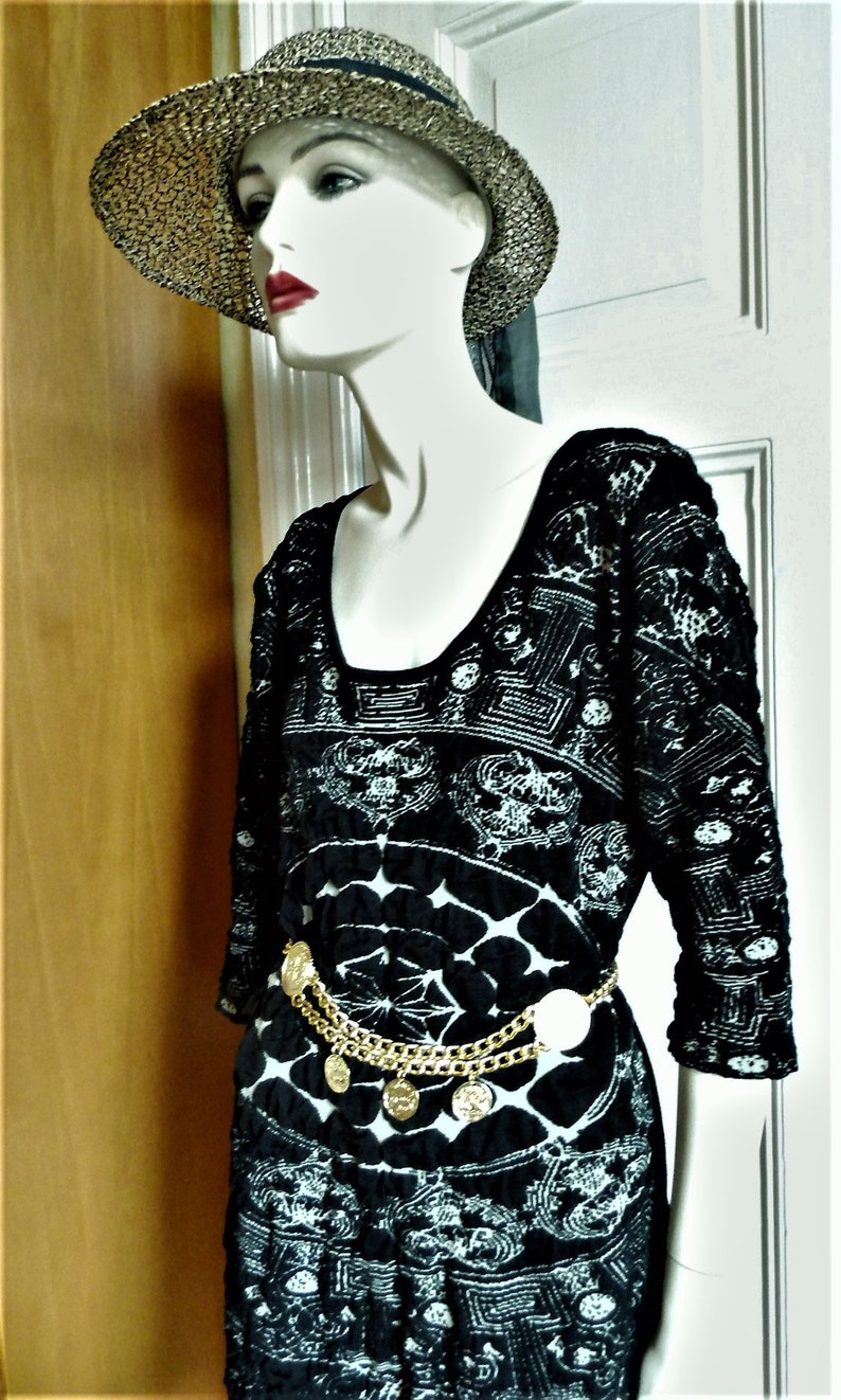 May include: A black and white patterned dress with a gold chain belt and a straw hat with a black ribbon.