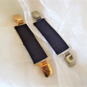 May include: Two black fabric braces with metal clips. One clip is gold and the other is silver.