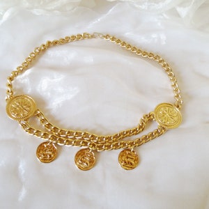May include: A gold chain belt with large round coin-shaped charms. The belt has two chains and four dangling charms.