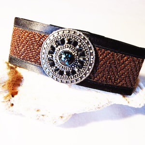 May include: A brown leather bracelet with a woven design and a silver circular charm with a turquoise stone in the centre.