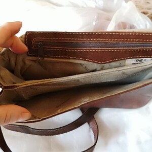 May include: A brown leather purse with a zippered pocket and a fabric lining. The purse has a strap and the text "THE TREND" is visible inside.