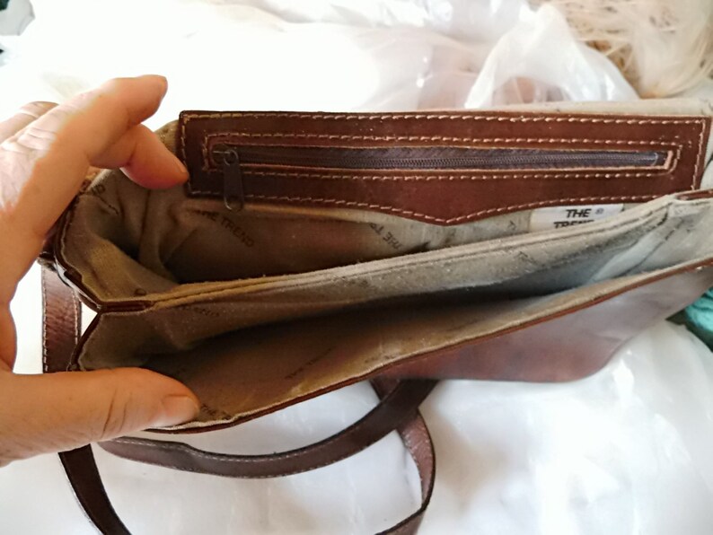 May include: A brown leather purse with a zippered pocket and a fabric lining. The purse has a strap and the text "THE TREND" is visible inside.