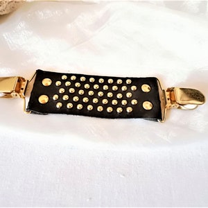 May include: A black leather suspender clip with gold-toned metal clips and studs.