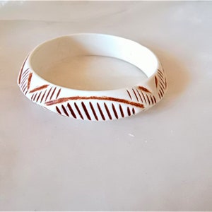 Op de afbeelding: Witte armband met een bruin geometrisch ontwerp.