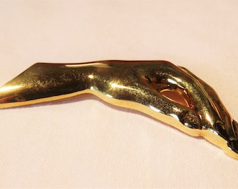 May include: A gold-toned metal brooch shaped like a hand, with the fingers curled inward, as if holding something.
