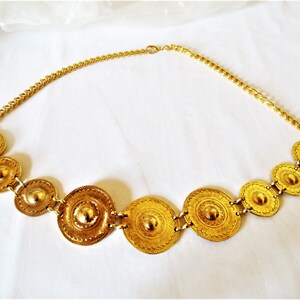 Puede incluir: Un collar de oro con una cadena y una serie de medallones redondos decorativos.