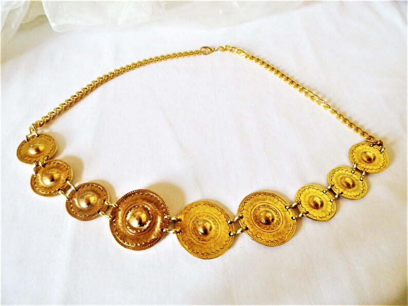 Puede incluir: Un collar de oro con una cadena y una serie de medallones redondos decorativos.