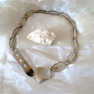 May include: A silver chain belt with a unique geometric design and a large, open buckle.